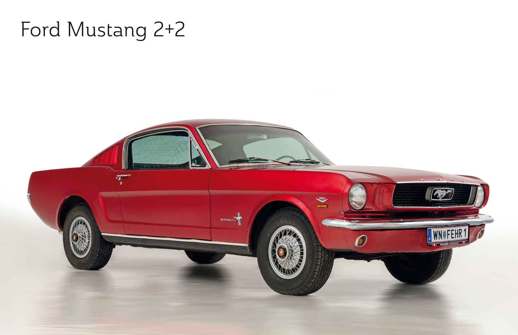 A red Ford Mustang 2+2 from the 1960s, photographed from the side on a white background.