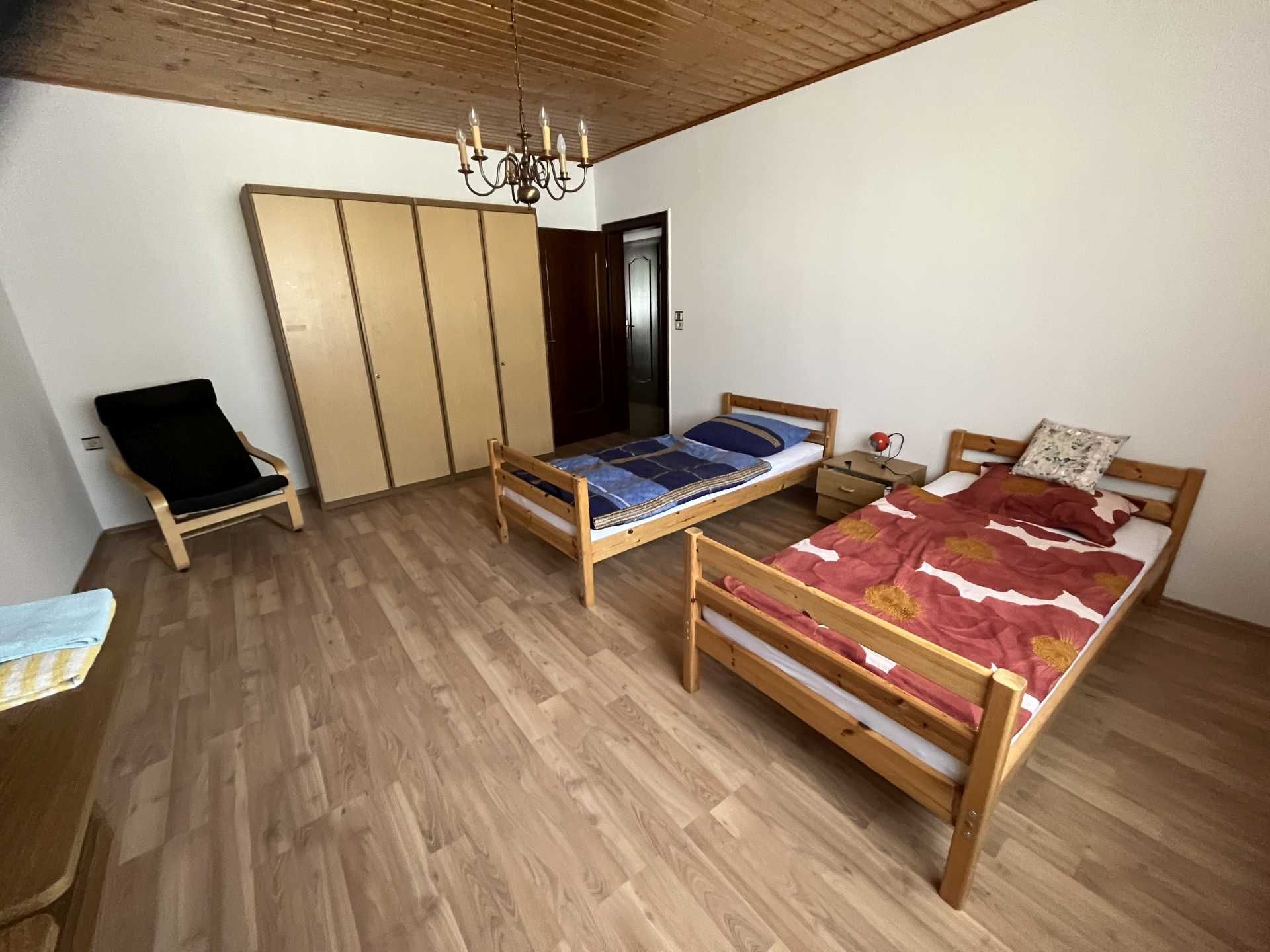 A simply furnished bedroom with two single beds, a closet and an armchair.