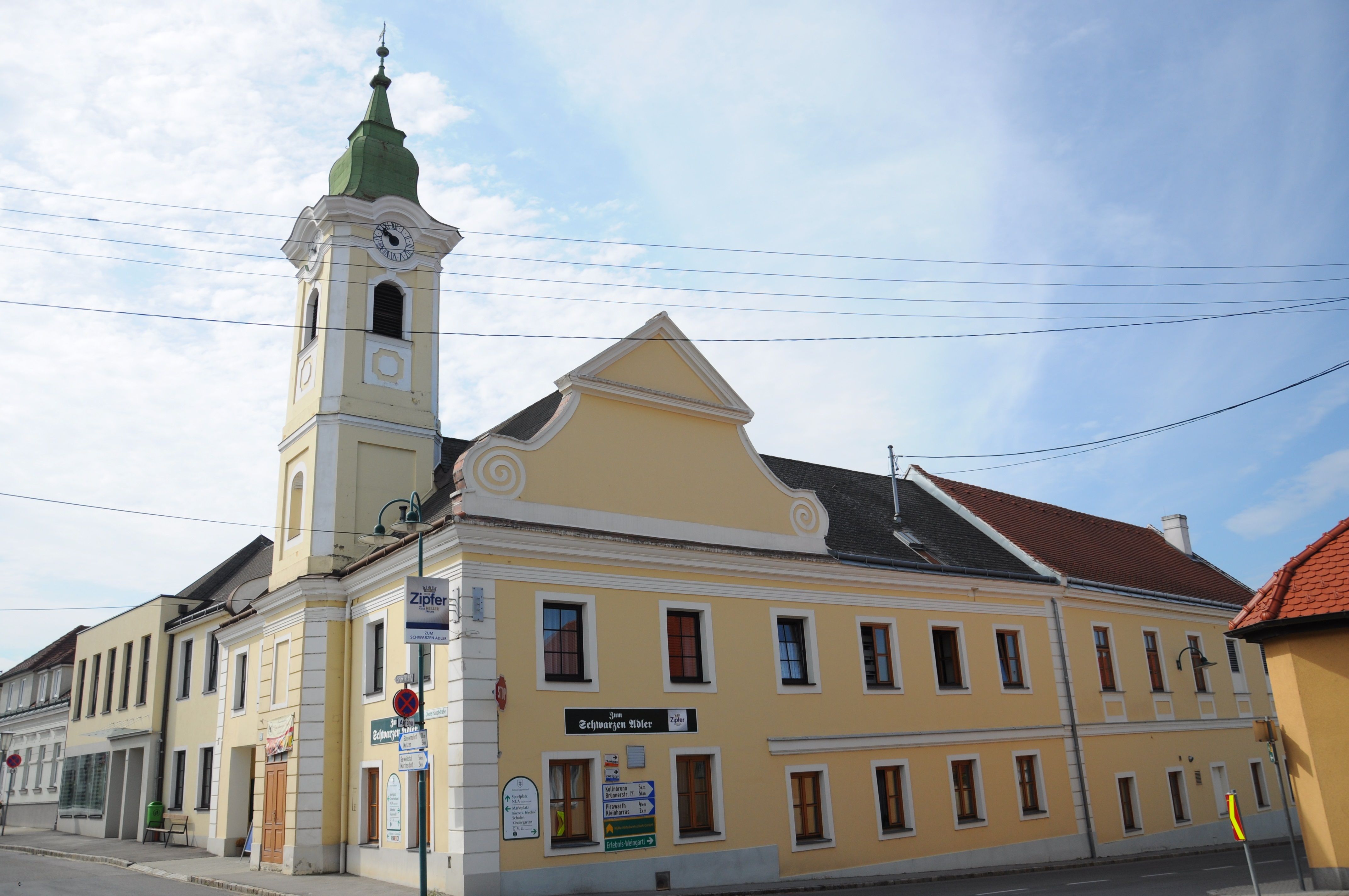 Yellow building with tower and clock, Gasthaus zum schwarzen Adler, blue sky.