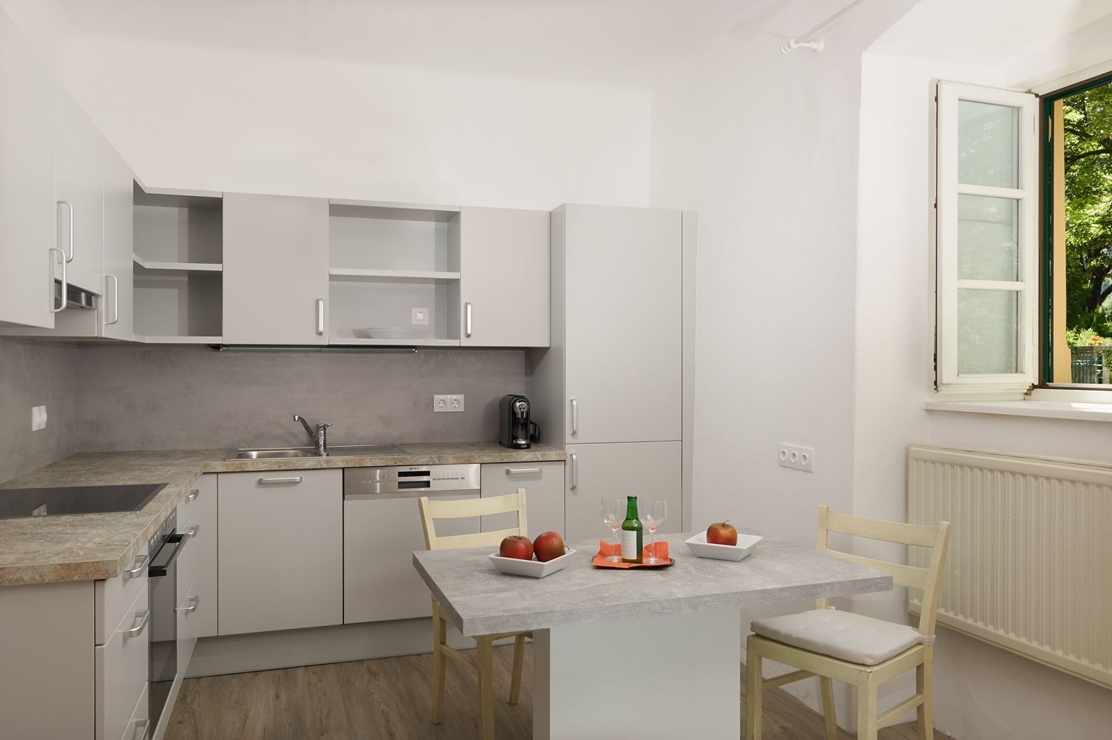 Modern kitchen with gray cabinets, table with apples and drink, open window.