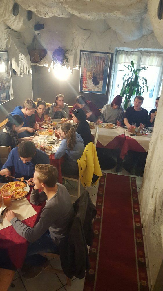 Group of people eating pizza in a cozy restaurant with cave walls.