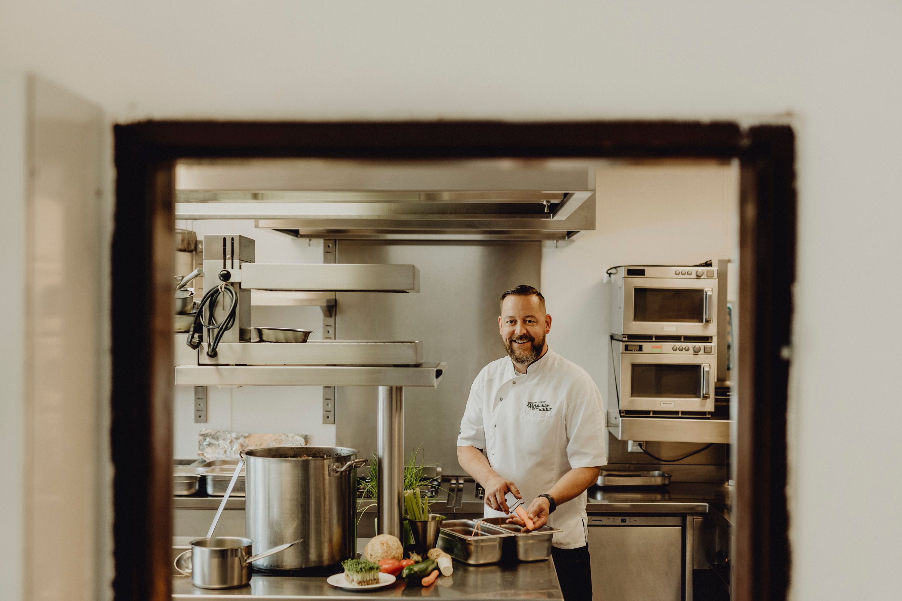 A chef in a professional kitchen, smiling as he cuts vegetables.