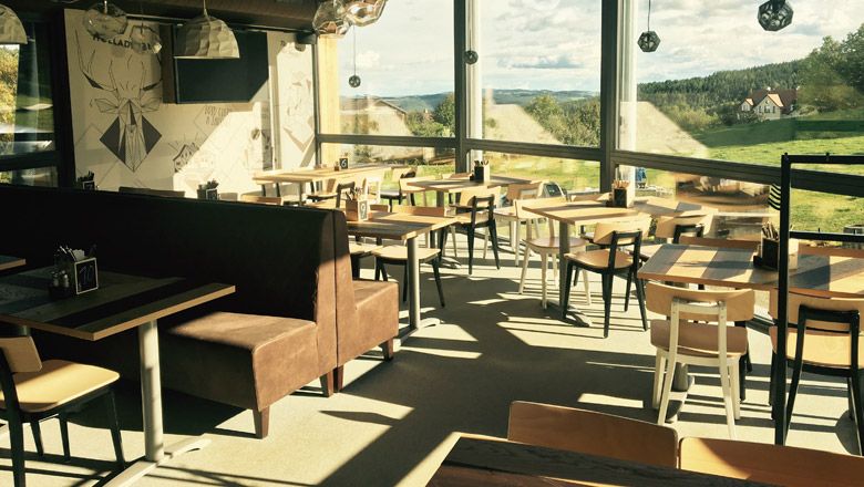 Interior view of the Wexl Lounge with tables and chairs, large windows with a view of the landscape.