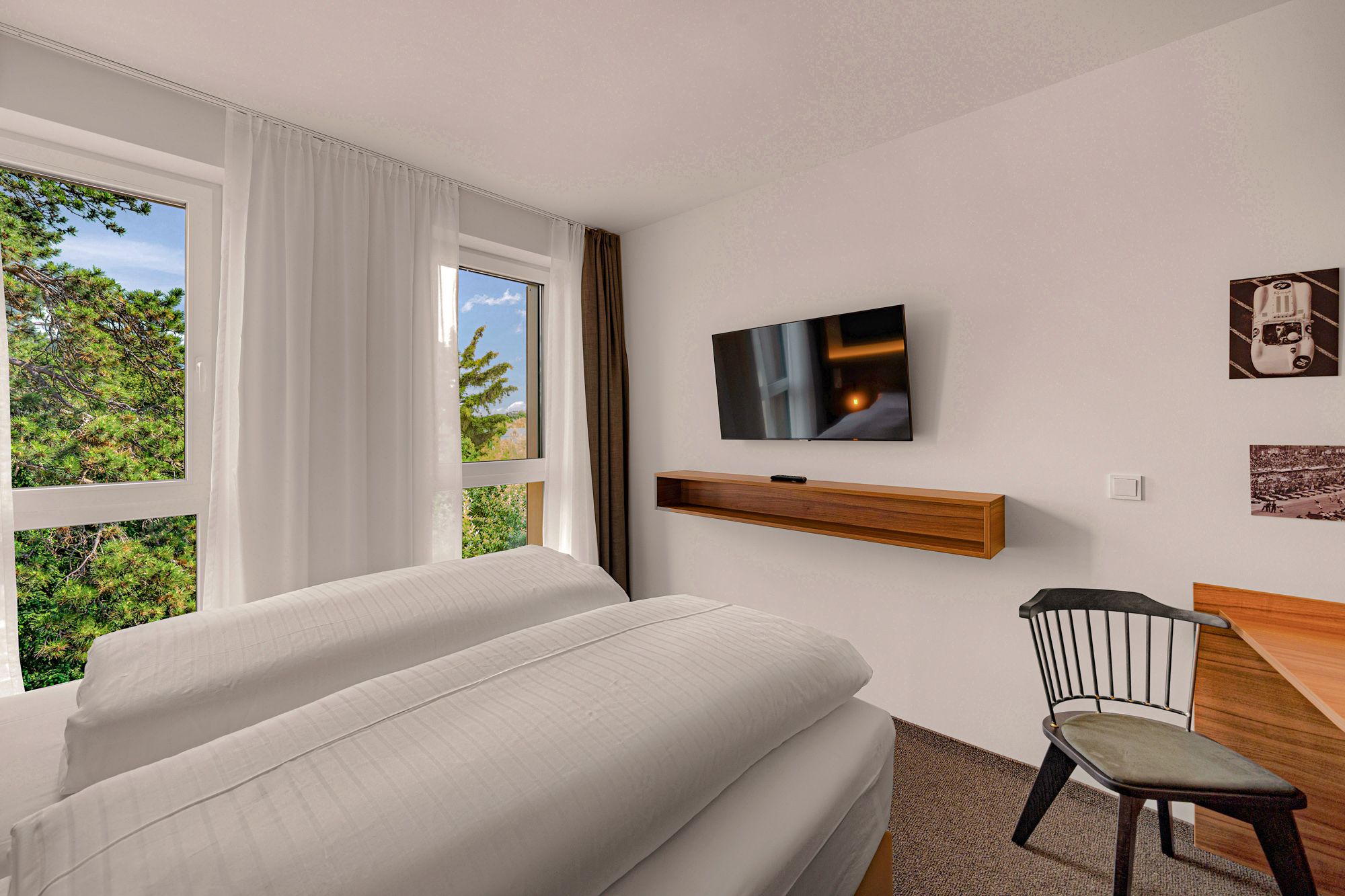 Modern hotel room with large bed, flat screen TV, desk and chair. Window with view of trees.