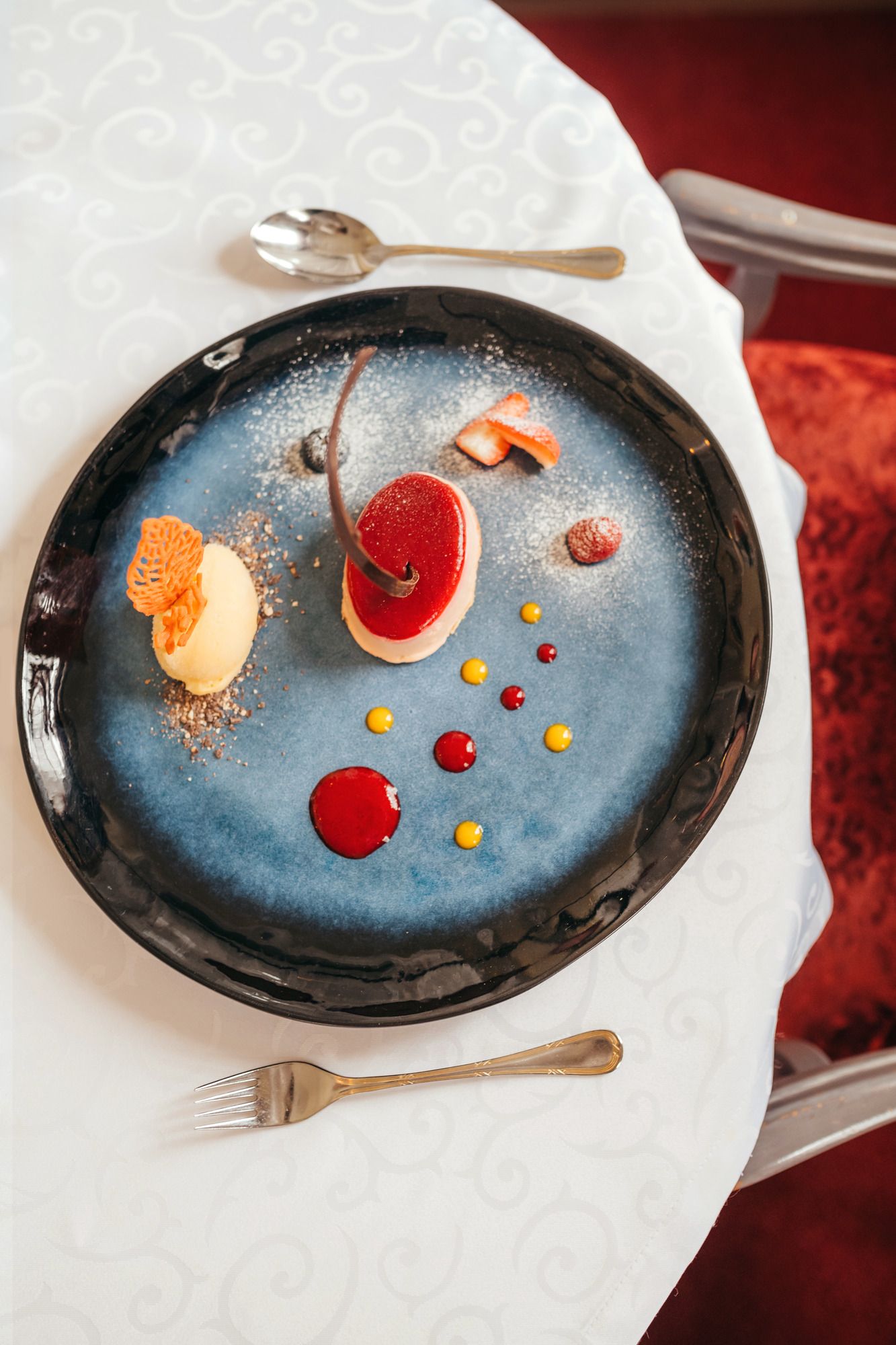 An artfully arranged dessert on a blue plate with red and yellow sauce dots.