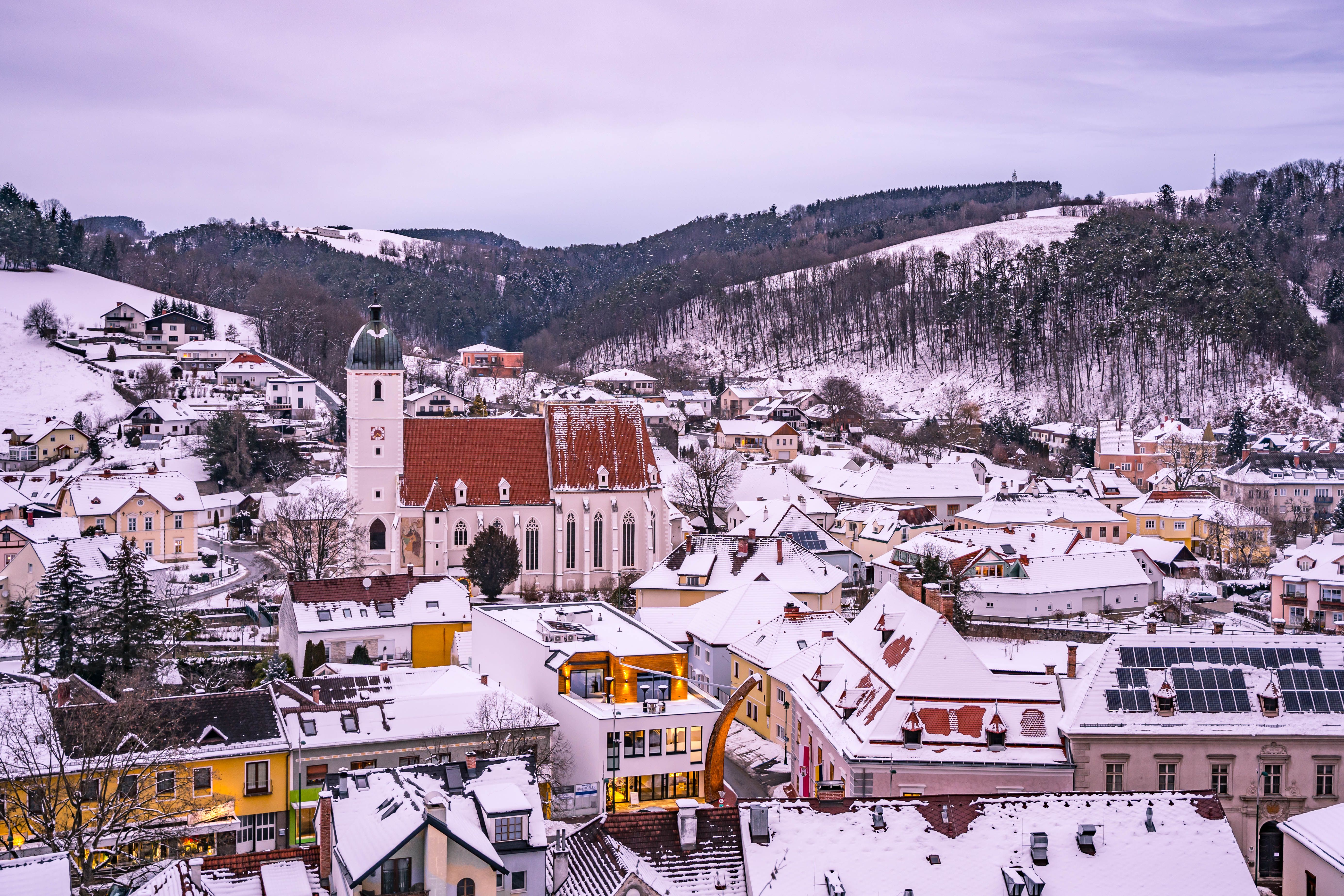 Winter view of Kirchschlag with snow-covered roofs and a church in the foreground.