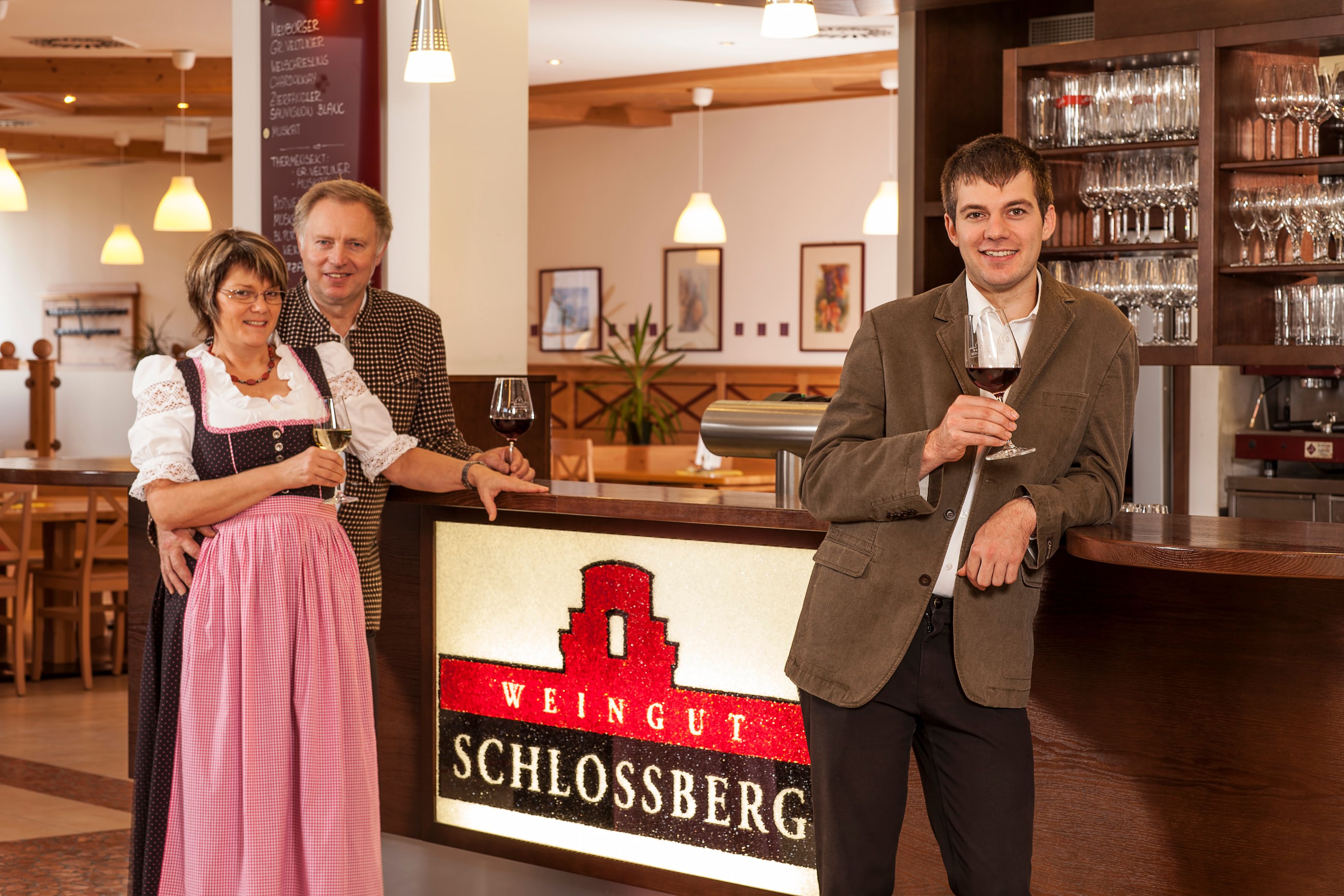 Three people stand at a bar in the Schlossberg winery with glasses of wine in their hands.