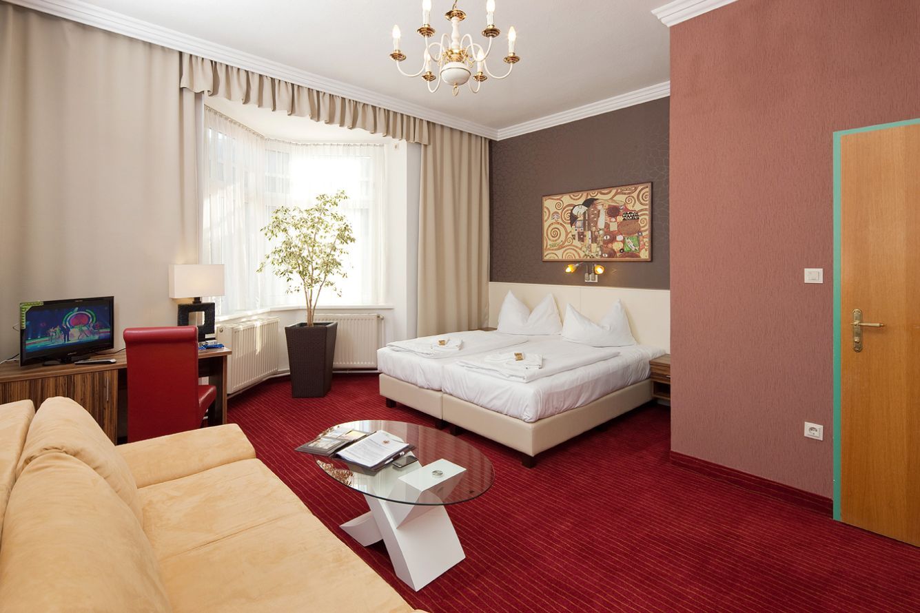 Hotel room with double bed, red carpet, sofa, TV and large window.