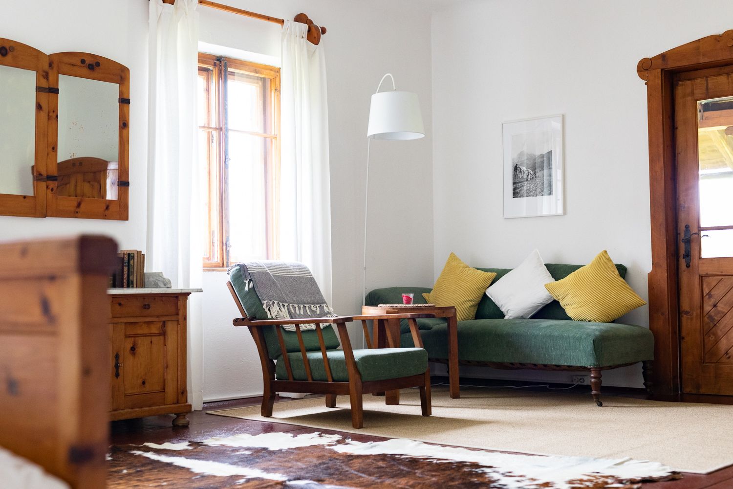Cozy living room with wooden furniture, green sofa, yellow cushions and cowhide carpet.