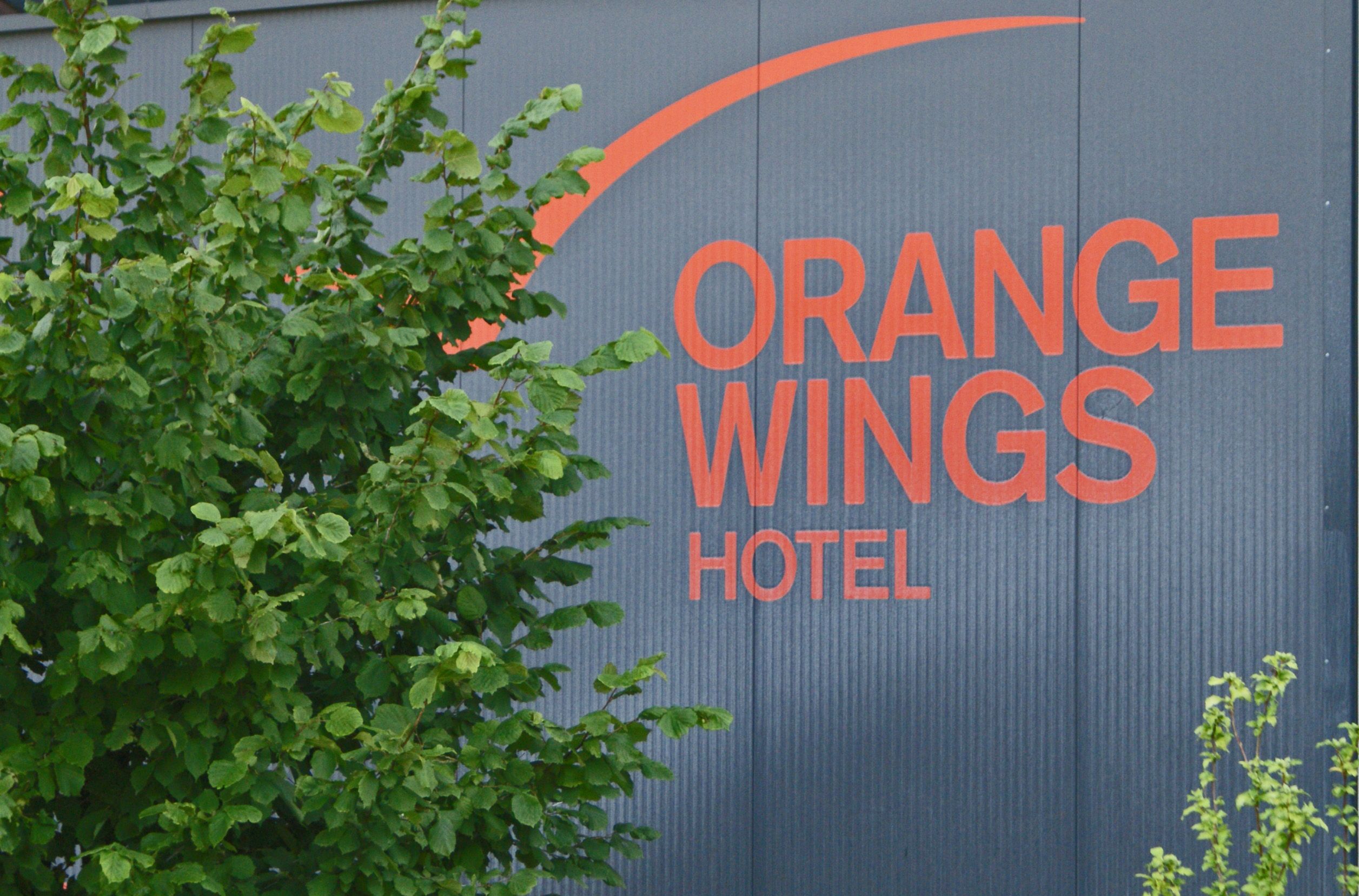 Logo of the Orange Wings Hotel on a wall with plants in the foreground.