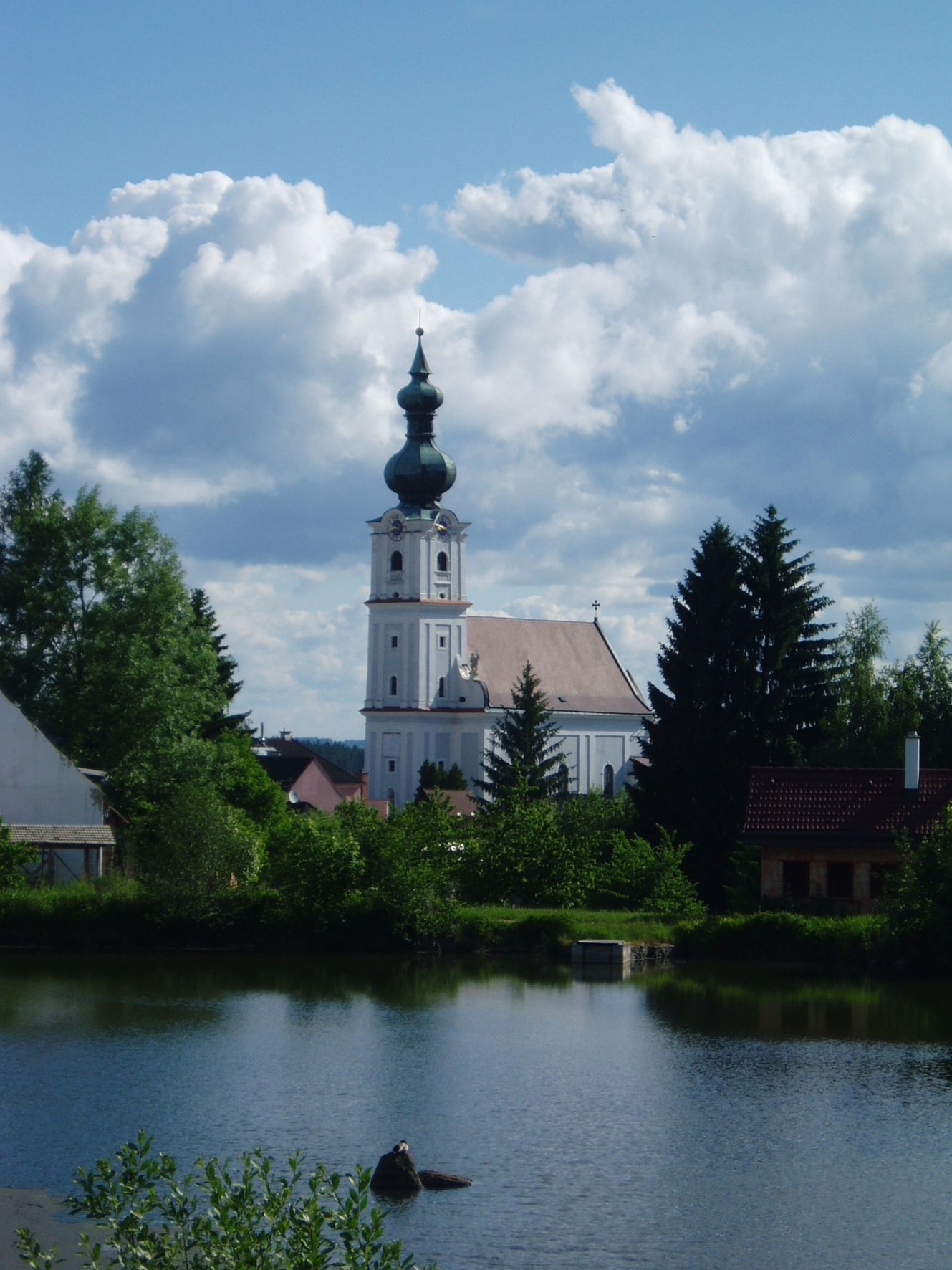 Church in Kirchberg am Walde with a pond in the foreground and a cloudy sky.