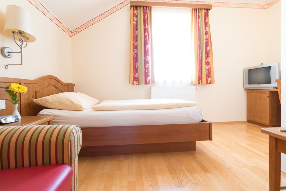 Single room with bed, TV and armchair.