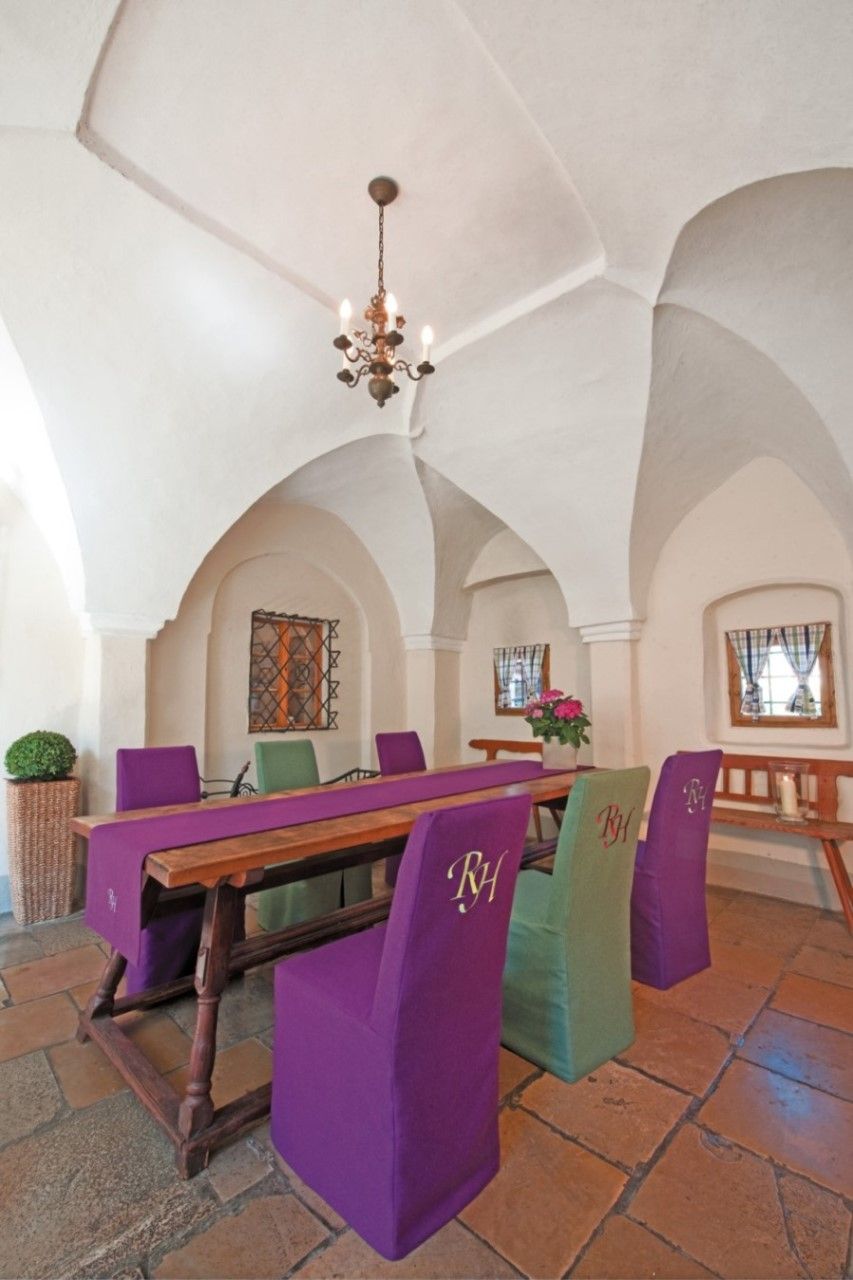 Interior view of a room in the Renaissance Hotel Raffelsberger Hof with vaulted ceiling, wooden table and chairs with purple and green upholstery.