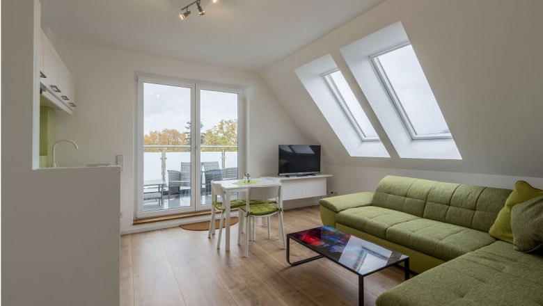 Modern living room with green couch, glass table, TV and balcony access.