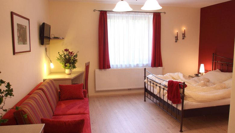 Comfortable hotel room with double bed, red sofa and desk.