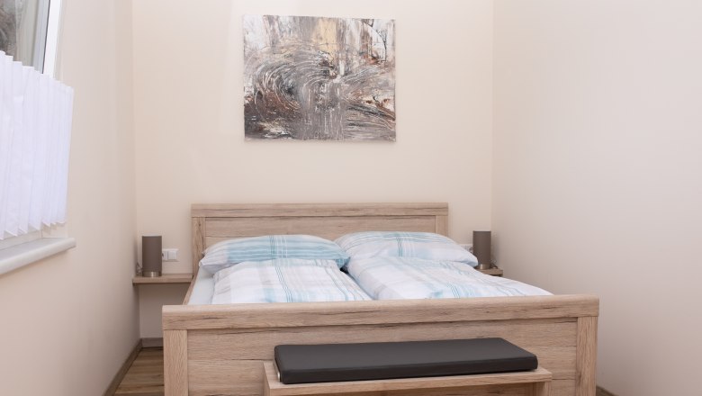 Bedroom with double bed, wooden furniture and abstract artwork on the wall.