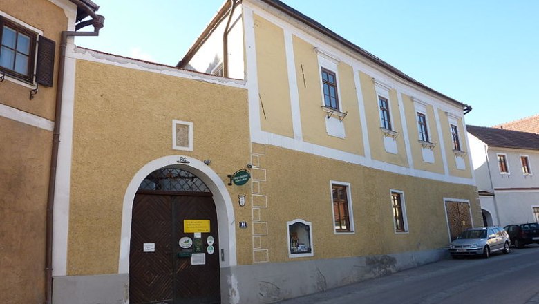 Manghof, © Heinrich Mang Yellow two-story building with wooden gate and windows in a street.