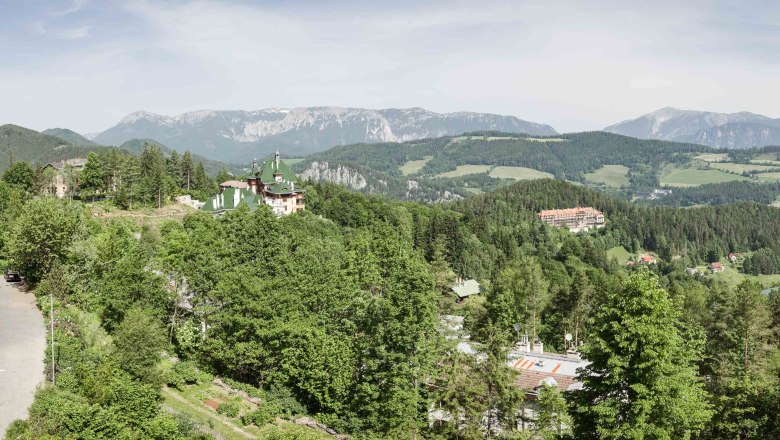 Panoramic view of a mountainous landscape with forest, road and buildings.