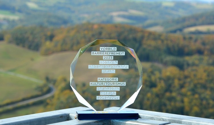 An award for accessibility 2023 stands on a railing with a landscape in the background. The viewing platform is accessible by elevator.