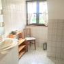 Bright bathroom with washbasin, wooden shelf, chair and window with curtains.