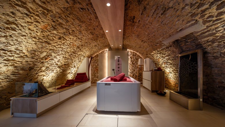 A stylish spa room with stone walls, a modern bathtub and red towels.
