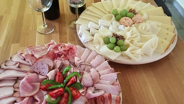 Two platters of cold cuts and cheese on a wooden table, decorated with grapes and tomatoes.