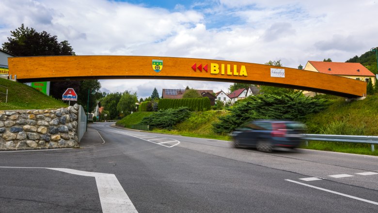 A wooden bridge with the lettering 'BILLA' spans a road in a rural setting.