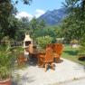 Garden area with wooden furniture and barbecue against a mountain backdrop.