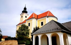 St. Nicholas parish church in Röschitz with yellow façade and red roof.