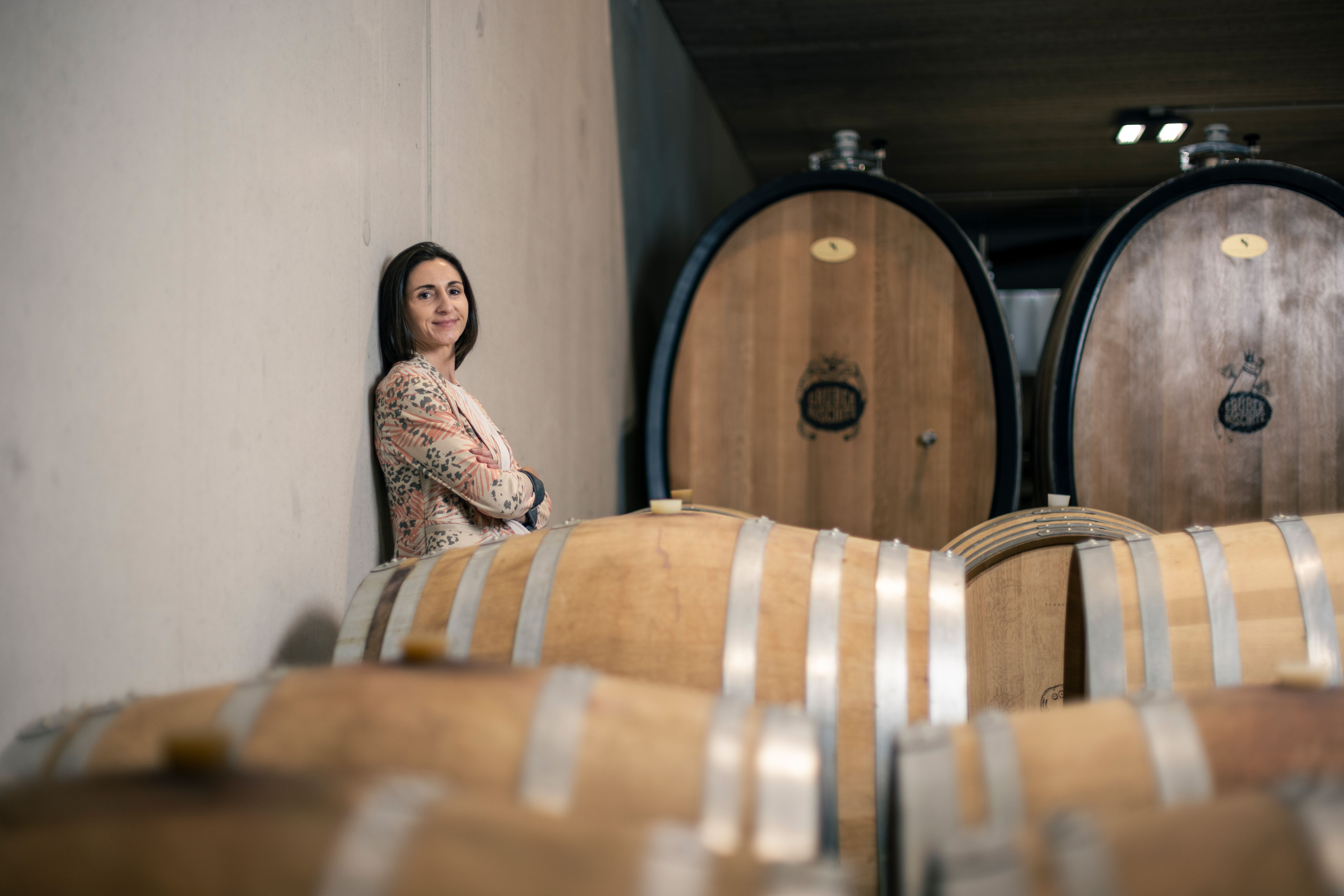 Woman leaning against a wall in a wine cellar with wooden barrels.