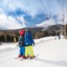Two children on skis use a drag lift in a snowy mountain landscape.