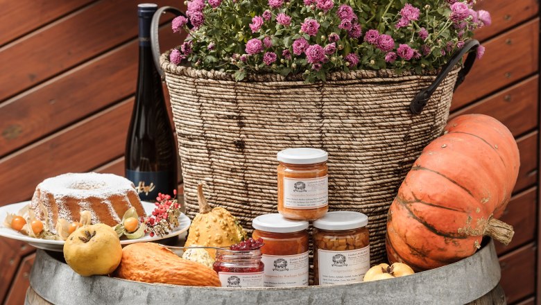 An arrangement of homemade specialties with pumpkin, jam, cake and flowers in a basket on a barrel.