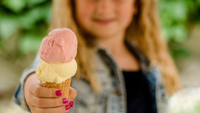 A child is holding an ice cream cone with two scoops, one pink and one yellow.