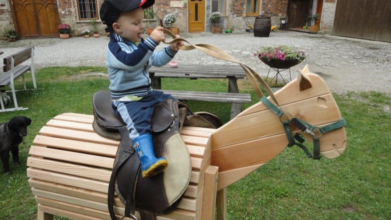 A child sits on a wooden toy horse outdoors.