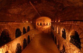 An atmospherically lit wine cellar with bottles stacked in niches along the walls.