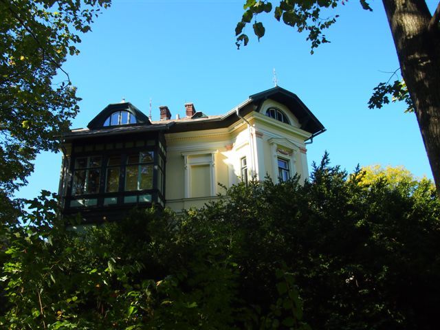 Historic villa behind trees, blue sky.