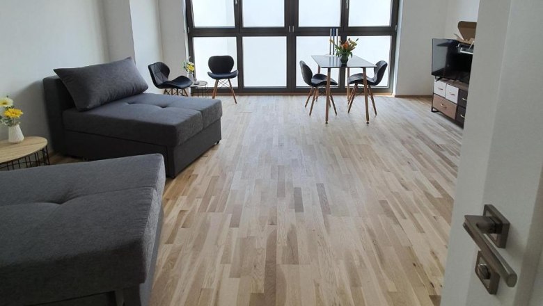 Modern room with wooden floor, gray sofas, dining table and large windows.