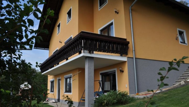 Yellow house with balcony and garden, surrounded by plants.