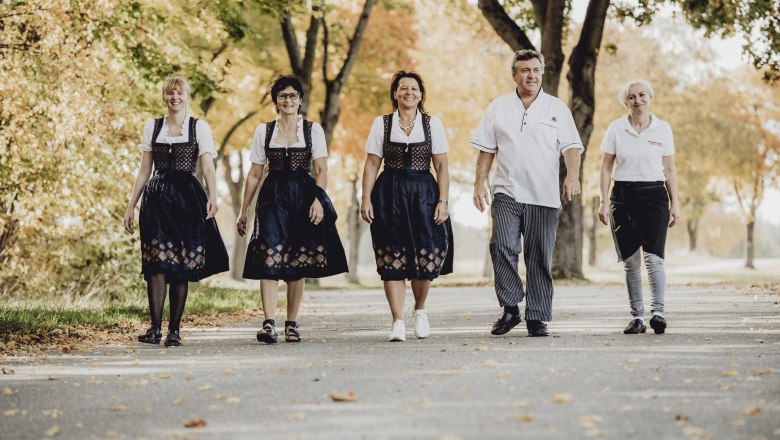 Five people in traditional dress walk along a tree-lined street.