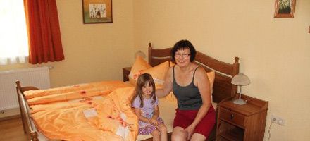 A woman and a child are sitting on a bed in a guest room with orange bed linen.