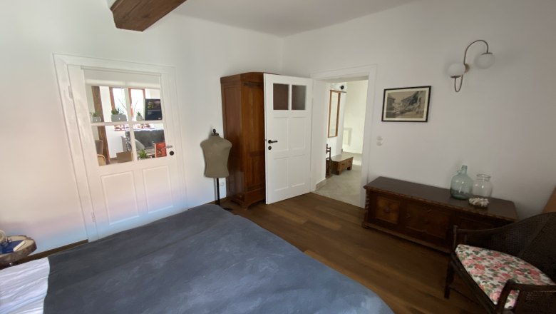 Bedroom with wooden floor, bed, closet, chest of drawers and chair.
