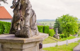 Stone statue on a pedestal with a green landscape in the background.