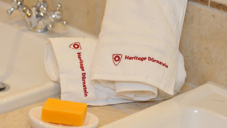 White towels with the inscription 'Heritage Dürnstein' next to a washbasin and a bar of soap.