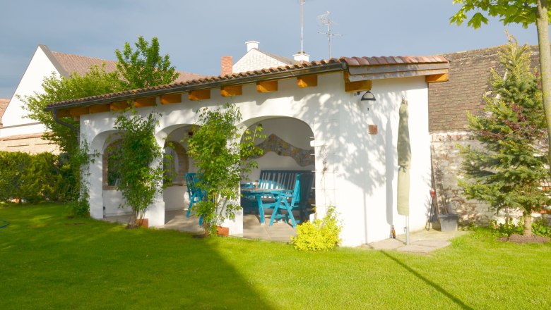 A garden with a covered terrace, blue furniture and green vegetation.