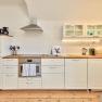 Modern kitchen with white cupboards, wooden worktop, stove, extractor hood and sink.