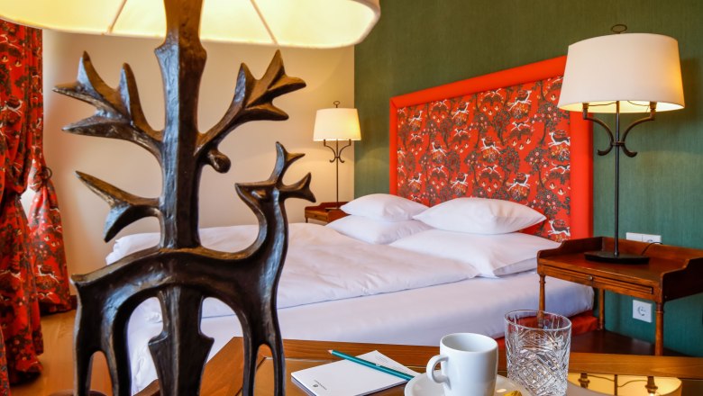 A stylishly furnished hotel room with a bed, decorative lamps and a table with a cup and glass.