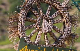 A woven straw wreath with a sign saying 'Ausg'steckt is' hangs from a chain.