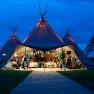 An illuminated tipi tent at night with festive decorations and guests inside.