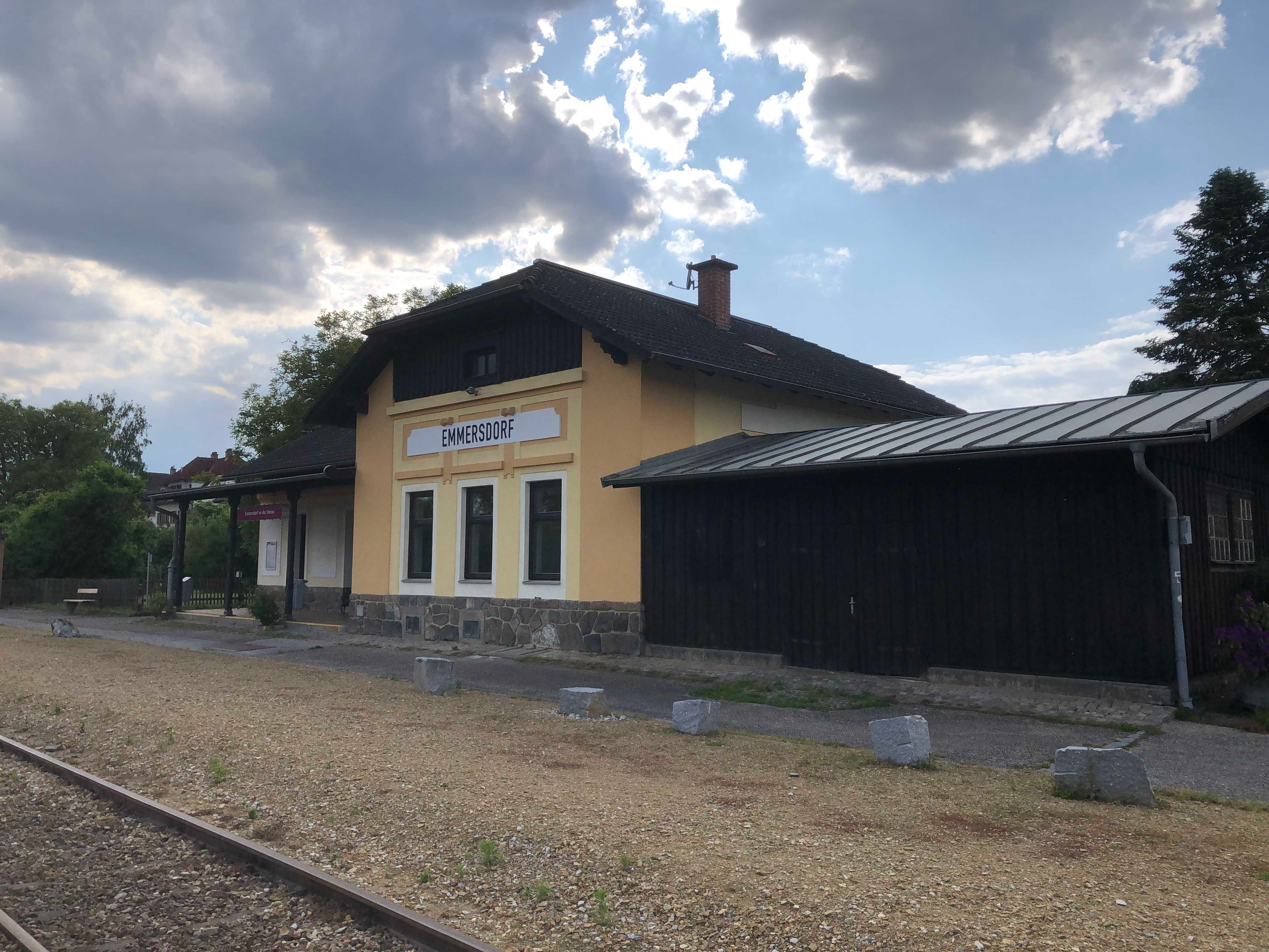 Emmersdorf station with yellow building and tracks in the foreground.