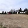Empty camper van site with a red car and trees in the background.